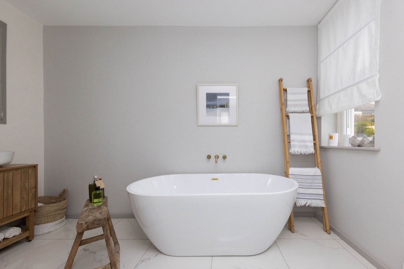 Freestanding bath beside a linen ladder and softly dressed window at The Lookout Brighton